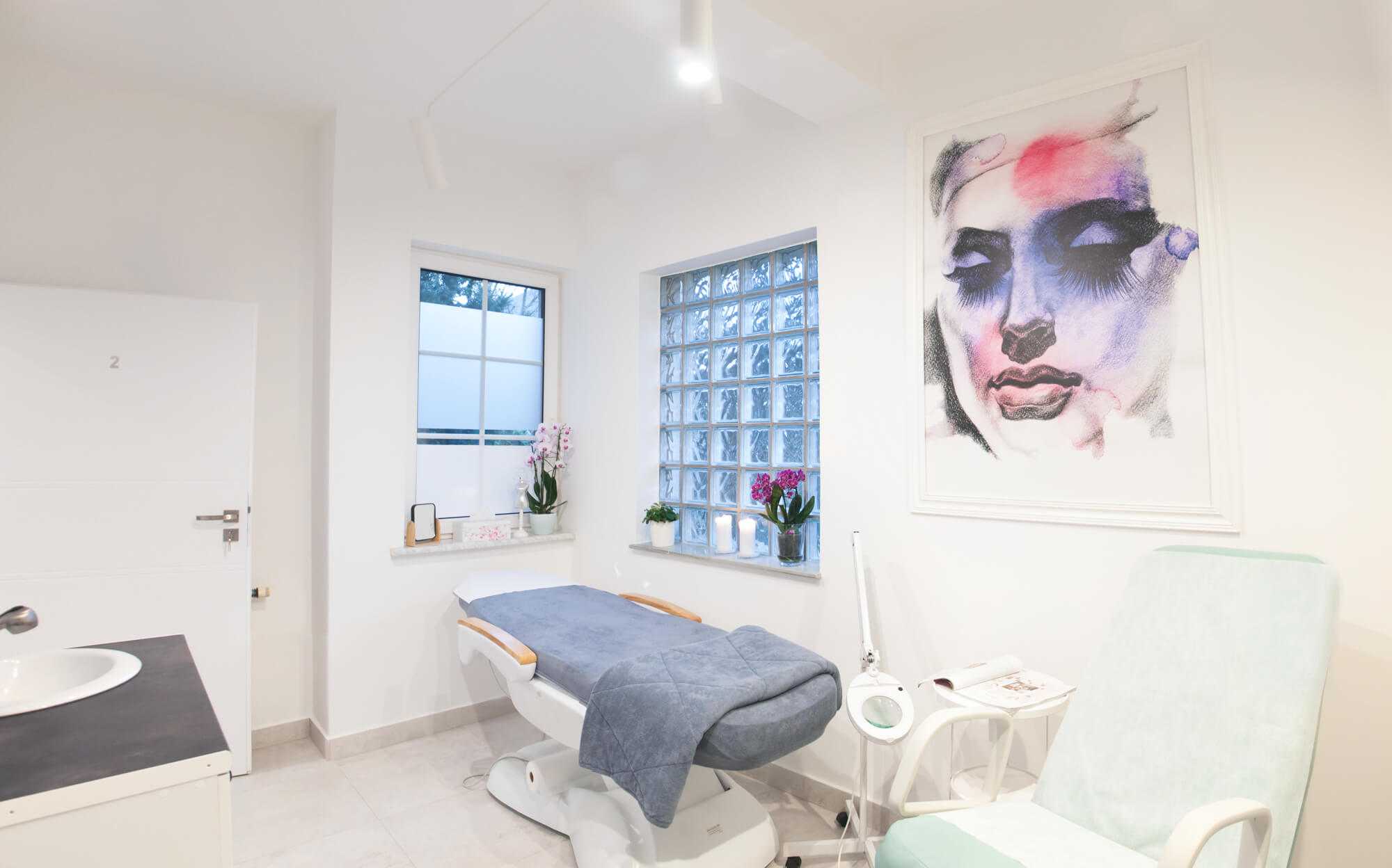 Białe wnętrze gabinetu w Salonie Kosmetycznym „Evita” z fotelem do masażu i fioletowo-różowym obrazem z twarzą kobiety